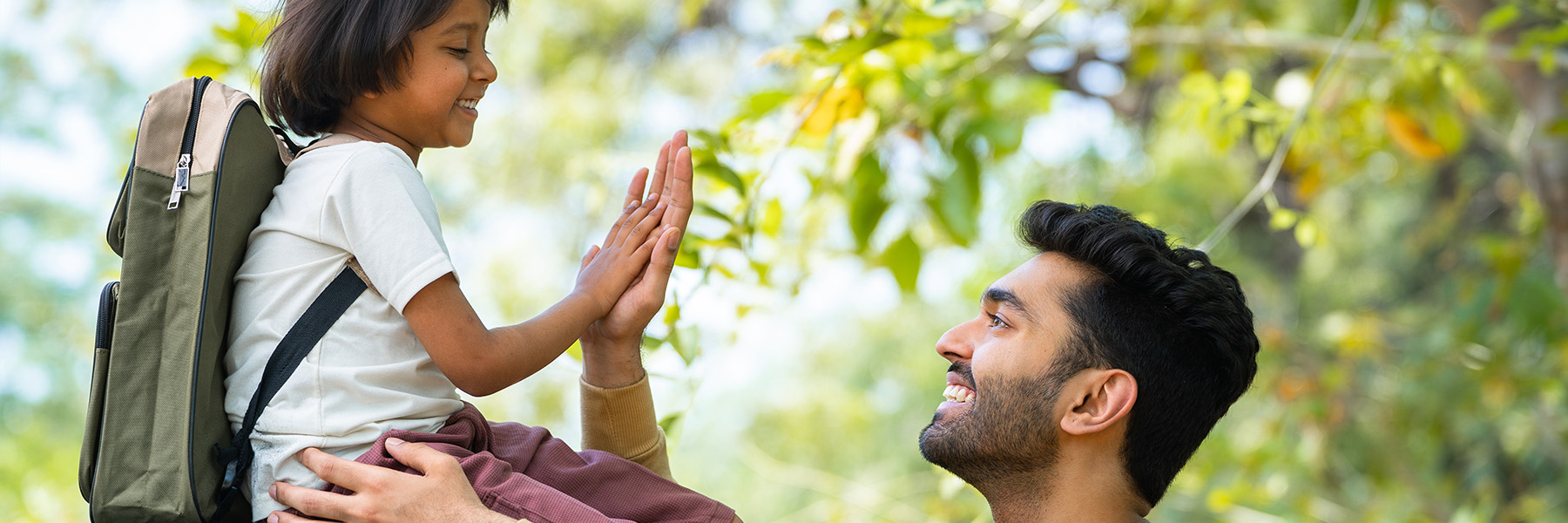 A parent high-fiving his child, who is wearing a backpack