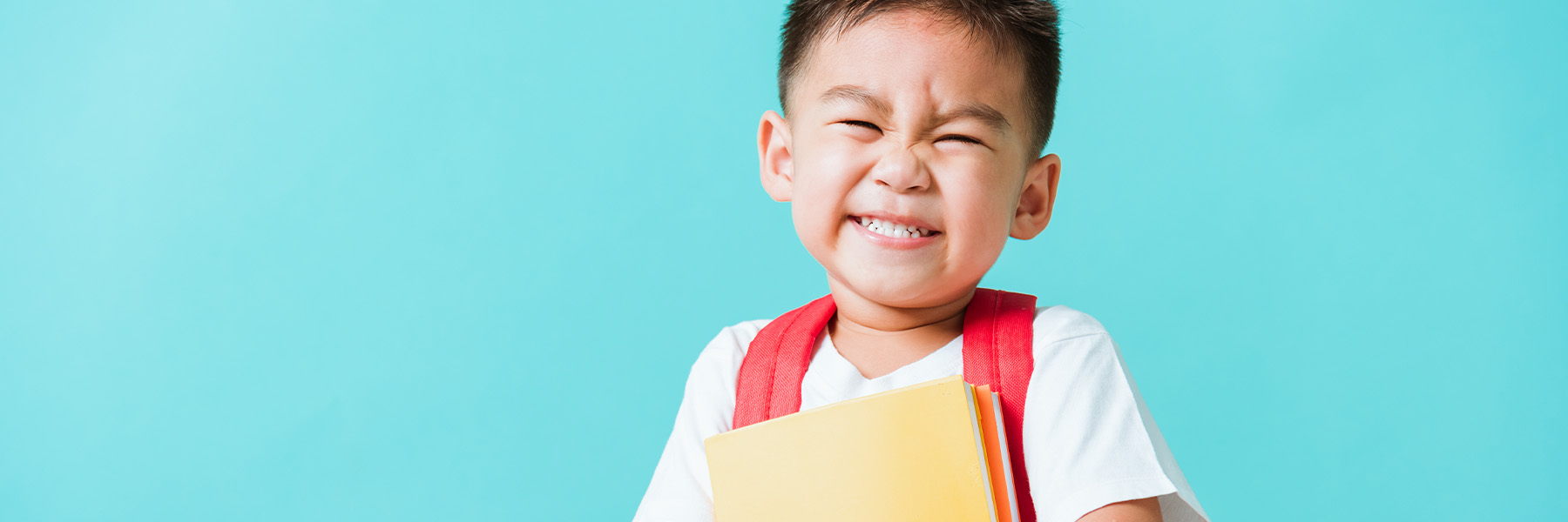 A child smiling with his backpack and school supplies on a blue background