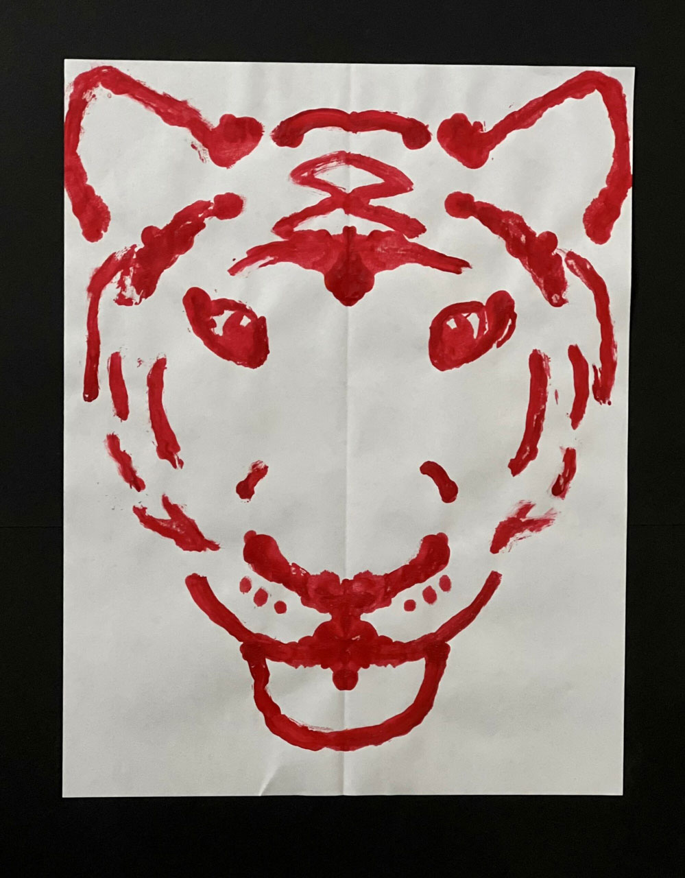 A painting of a tiger in red on a white piece of paper.